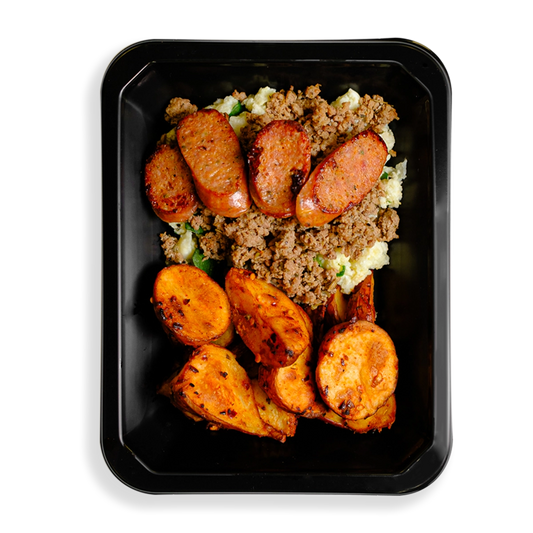 A colorful meal featuring seasoned ground turkey with a golden-brown sear, resting atop fluffy white scrambled egg whites mixed with wilted green spinach. On the side, crispy roasted red potatoes with a caramelized edge add texture, while slices of bison jalapeño cheddar sausage, speckled with melted cheese and bits of green jalapeño, crown the dish with a bold, savory finish. All this fills a black takeout container and is for those who are sometimes too busy to cook but want to still eat delicious food.