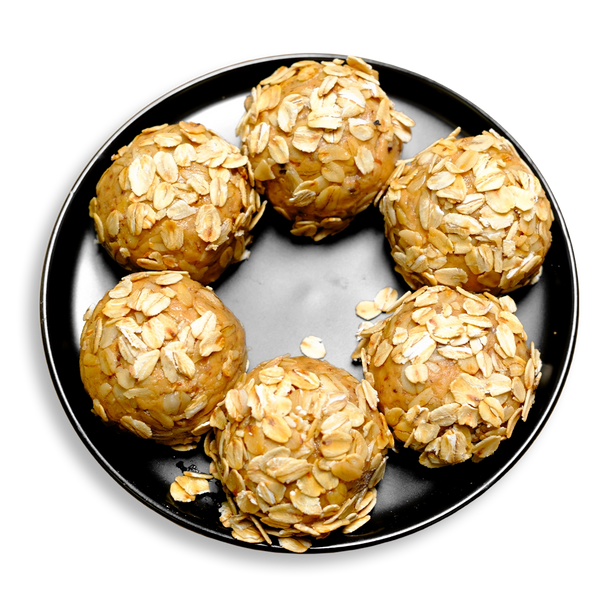 A black plate displays six round peanut butter protein balls, each rolled in a generous layer of toasted rolled oats. These all-natural bites are made from a nutrient-rich blend of peanut butter, whey protein, coconut flour, and ground flaxseed, making them a convenient, high-protein healthy meal prep snack ideal for fitness-focused health food lovers.