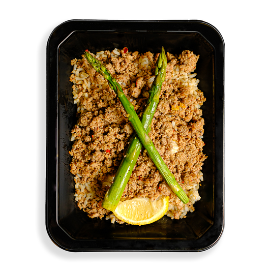 a container if filled with ground turkey over rice and two stalks of asparagus and a lemon wedge sit atop this delicious mixture of food. the togo meal container indicates that this is a health prepared meal designed for someone loosing weight or bulking up.
