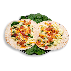 Two soft flour tortillas lay open on a bed of fresh spinach leaves, each filled with a vibrant mix of fluffy scrambled egg whites, finely chopped spinach, and crispy bacon bits. A sprinkle of cheddar jack cheese adds a melted, savory finish to this high-protein, low-carb healthy prepared meal: perfect for easy breakfast meal prep or a quick, energizing snack.