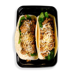 two tacos sit in a black togo container that can barely fit all this delicious looking food. Yellow and white shredded cheese sits atop ground pork which is on top of some leafy green greens.  This healthy prepared meals looks appetizing for any occasion and for people who want to watch what they eat.