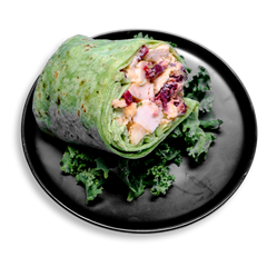 A vibrant health food wrap featuring tender diced Creole-seasoned chicken, tangy Greek yogurt, and sweet dried cranberries, all wrapped in a toasted spinach tortilla. Hints of fresh celery and aromatic tarragon peek through, with the wrap cut in half and nestled on a bed of leafy kale—an ideal healthy meal prep for those seeking flavor-packed nutrition.