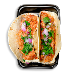 Two soft flour tortillas are neatly packed in a black to-go container, each filled with shredded chicken thighs tossed in a bold, spicy tomato-chipotle tinga sauce. The tacos are garnished with vibrant chopped red onions and fresh cilantro, offering a colorful and flavor-packed healthy prepared meal. This high-protein health food option is ideal for healthy meal prep, delivering authentic taste and clean ingredients in a convenient, ready-to-eat format.