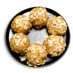 A black plate displays six round peanut butter protein balls, each rolled in a generous layer of toasted rolled oats. These all-natural bites are made from a nutrient-rich blend of peanut butter, whey protein, coconut flour, and ground flaxseed, making them a convenient, high-protein healthy meal prep snack ideal for fitness-focused health food lovers.