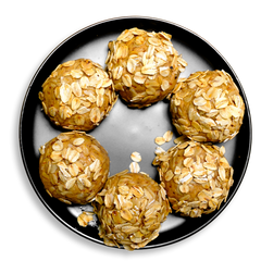 Top-down view of six golden oat-coated energy bites neatly arranged on a black dish. Made with creamy peanut butter, flaxseed, MyFitFoods whey protein, and a hint of chocolate chips, these soft and chewy treats offer a clean, satisfying option for healthy prepared meals or on-the-go snacking.