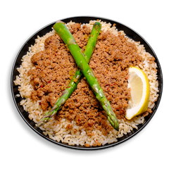 A healthy prepared meal featuring a generous serving of lean ground turkey, seasoned with creole spices, lemon pepper, and garlic, resting atop a bed of fluffy parboiled brown rice. Two vibrant asparagus spears are artfully placed in an “X” on top, with a fresh lemon wedge tucked in the corner for a citrusy finish. A visually appetizing, protein-packed health food option ideal for clean eating and meal prep.