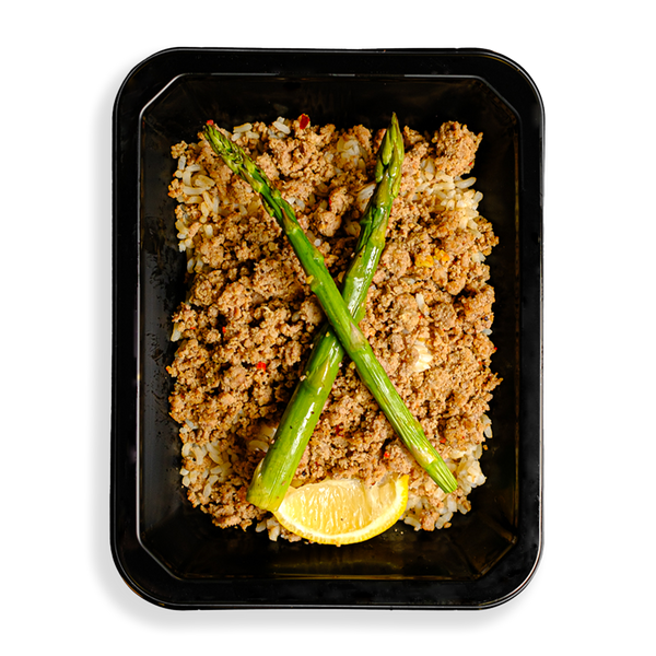 a container if filled with ground turkey over rice and two stalks of asparagus and a lemon wedge sit atop this delicious mixture of food. the togo meal container indicates that this is a health prepared meal designed for someone loosing weight or bulking up.
