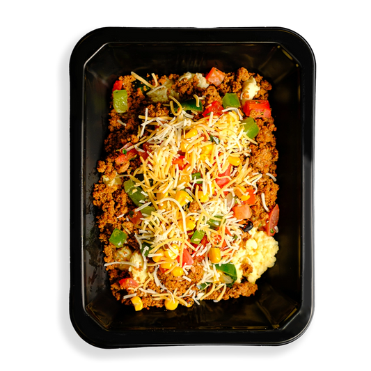 A colorful mound of lean turkey, eggs, corn, and peppers topped with melted cheddar and fresh tomatoes, perfect for health-focused eaters on the go. This food sits inside a black togo container and is clearly ready to be delivered and enjoyed.