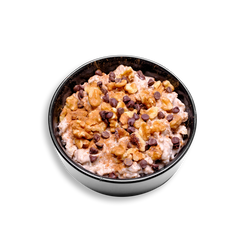 A hearty black colored bowl of protein-rich oatmeal sits in a black dish, thick and creamy from slow cooking in almond and coconut milk. The surface is generously sprinkled with crunchy chopped walnuts, melty chocolate chips, and a dusting of cinnamon, creating a visually inviting and nutrient-dense healthy prepared meal perfect for meal prep or a clean, energizing breakfast.