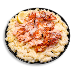 A savory and satisfying healthy meal prep plate showcasing golden, flaky salmon shredded over gluten-free pasta spirals. The dish is bathed in a luscious Alfredo sauce and spiced with hints of chili, lemon, and garlic, creating a perfect balance of creamy and zesty flavors—health food that feels indulgent but is made to nourish.
