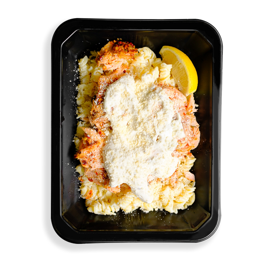 A pale, creamy salmon pasta with flakes of spice-rubbed Atlantic salmon over brown rice noodles, topped with parmesan and a light Alfredo sauce filling the black togo container.  This looks to be a hearty prepared meal designed for health conscious people who love eating.