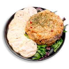 A creamy mound of salmon dip made with Atlantic salmon, Greek yogurt, and cream cheese sits atop a bed of fresh spring greens. The dip is topped with a sprinkle of dill and surrounded by a neat fan of round, gluten-free crackers. This high-protein, omega-3-rich healthy prepared meal offers a savory option perfect for clean snacking or a light meal to share with friends or family.