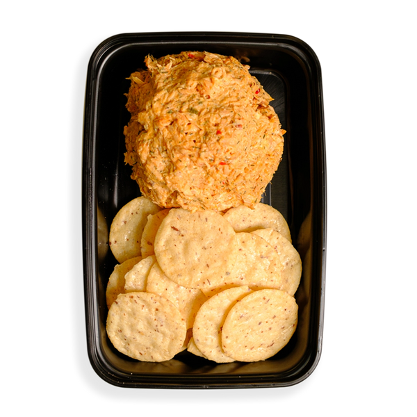 A large portion of shredded salmon with other tasty ingredients occupy half the black togo container with flavor while the remaining half contains very healthy looking crackers that are all in the shape of perfect circles.  This appears to be the perfect healthy snack for busy people on the go.