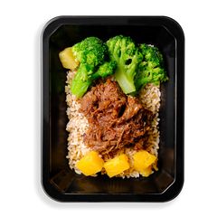 Vibrant green broccoli pulled beef and pineapple chunks sit on top of a bed of brown rice in a black to-go food container.  This meal is obviously focused on being extremely healthy while not sparring flavor.  The container that this food is in must be for a health food delivery services or a store where you can pick up healthy prepared meals.